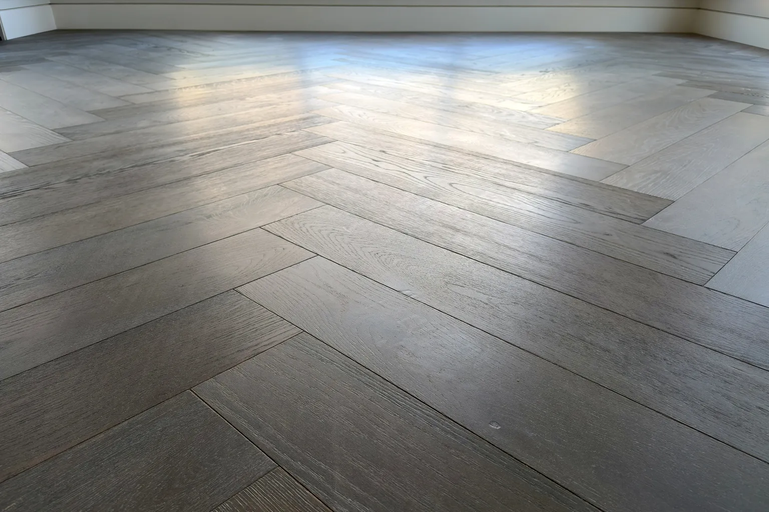 A herringbone timber floor laid through an empty room, with the light running along the boards